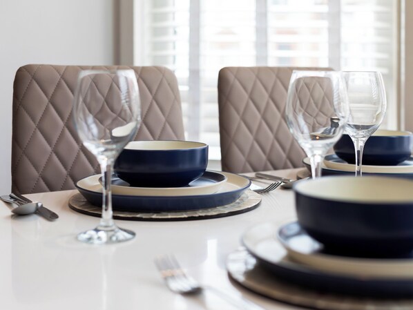 A dining table set with blue and beige plates, bowls, and wine glasses, with a window in the background.