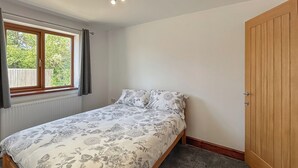 En säng för en person med ett blommigt överkast i ett rum med en garderob i trä och ett fönster med gardiner.