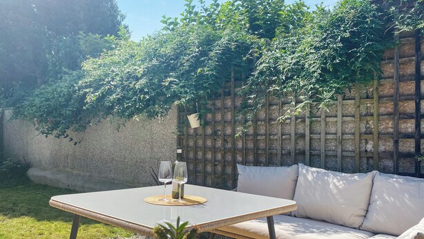 A patio with a table, two wine glasses, and a bottle, surrounded by greenery and a wooden fence. - 4 bedroom accommodation in St Agnes (St Agnes)