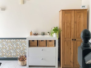Ein Zimmer mit weißem Schminktisch, Korbwannen, einer Topfpflanze und einem Holzschrank.
