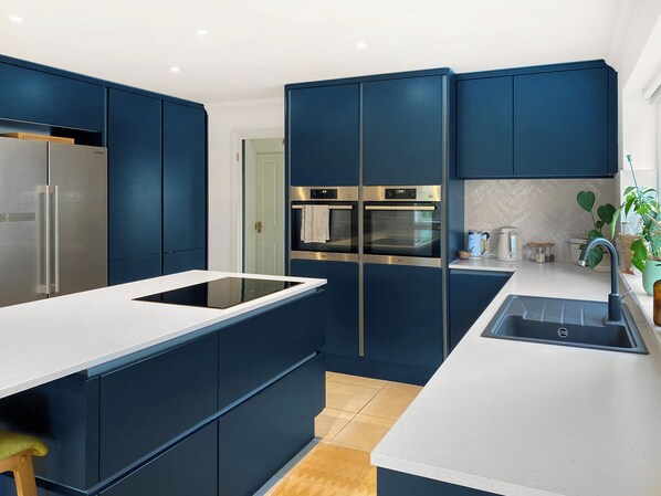 A modern kitchen with dark blue cabinetry, stainless steel appliances, a white countertop, and a sink.