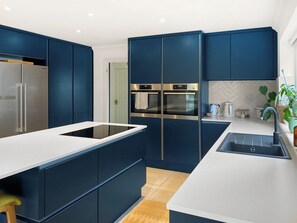 Una cocina moderna con armarios azul oscuro, electrodomésticos de acero inoxidable, encimera blanca y un lavabo.