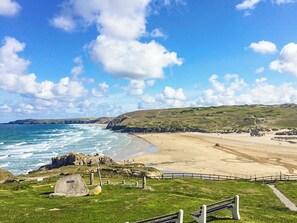 A coastal landscape with a beach, grassy areas, and rocky outcrops.