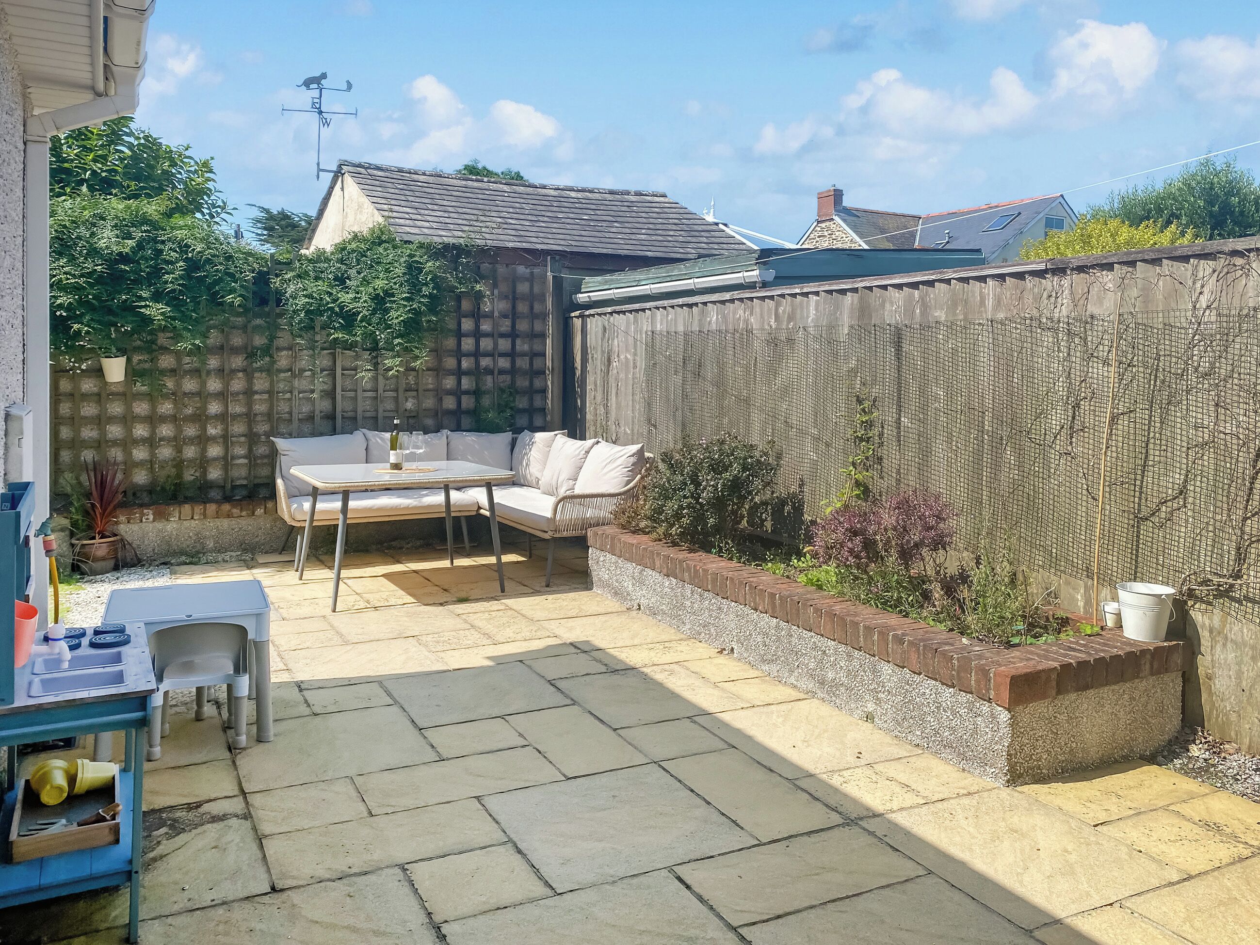 Een terras met een tafel en stoelen, een houten schutting en een bloembed met planten.