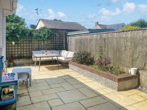 A patio with a table and chairs, a wooden fence, and a garden bed with plants.
