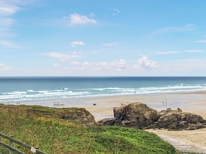 A coastal landscape with a beach, ocean waves, rocky outcrops, and a clear sky.