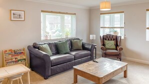 A living room with a leather sofa, a wooden coffee table, a small table with children's books, and a chair. - 4 bedroom accommodation in St Agnes (St Agnes)