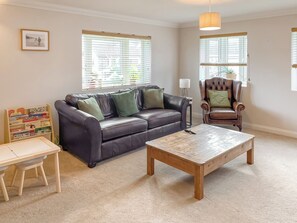 A living room with a leather sofa, a wooden coffee table, a small table with children's books, and a chair.
