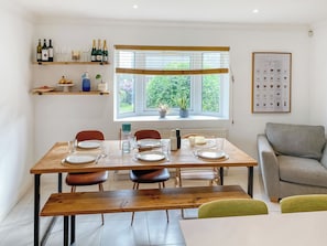 A dining area with a wooden table set for four, chairs, a bench, a sofa, and a window with blinds.