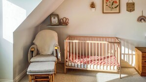 A room with a crib, a cushioned chair, a wooden cabinet, and a sloped ceiling. - 4 bedroom accommodation in St Agnes (St Agnes)