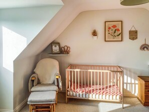 A room with a crib, a cushioned chair, a wooden cabinet, and a sloped ceiling.