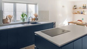 A modern kitchen with a large island, a window with plants, and a wine rack. - 4 bedroom accommodation in St Agnes (St Agnes)
