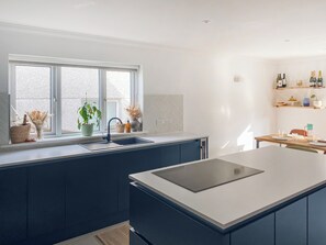 A modern kitchen with a large island, a window with plants, and a wine rack. - 4 bedroom accommodation in St Agnes (St Agnes)