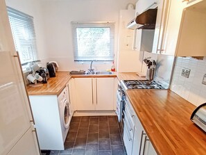 A compact kitchen with a washing machine, a sink, and a stove. - 2 bedroom accommodation in Brixham (Brixham)