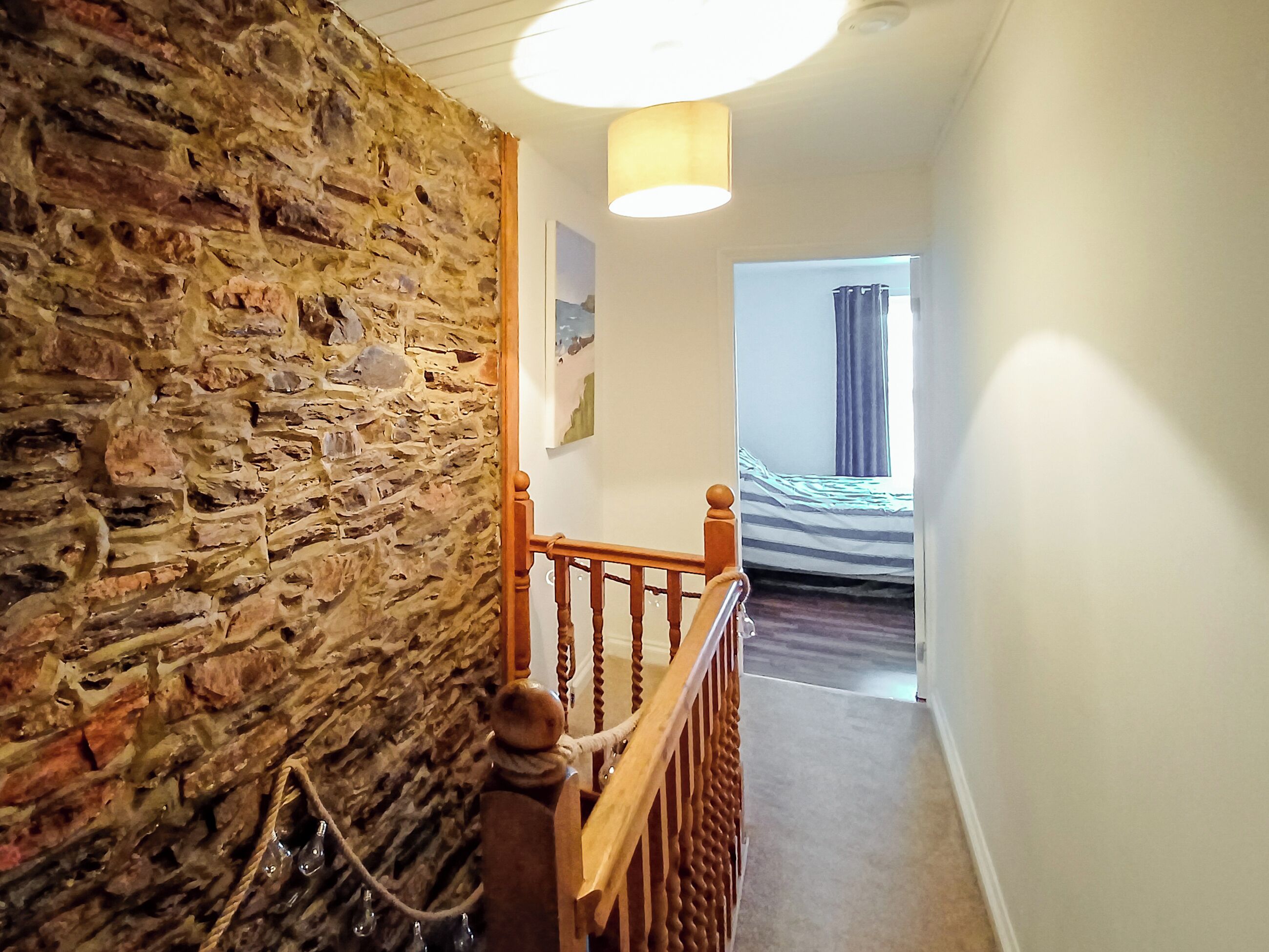 A staircase leading to a bedroom with a stone wall, a hanging light fixture, and a bed with a window.