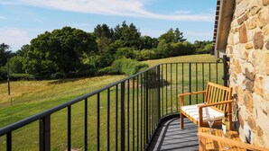 A balcony with a stone wall, a wooden chair, and a view of a grassy field and trees. - 1 bedroom accommodation in Shropshire (Shropshire)