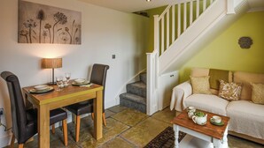 A dining area with a wooden table and chairs, a painting on the wall, and a staircase leading to a green room. - 1 bedroom accommodation in Shropshire (Shropshire)