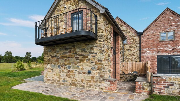 A stone building with a balcony, a brick extension, and a paved patio area. - 1 bedroom accommodation in Shropshire (Shropshire)