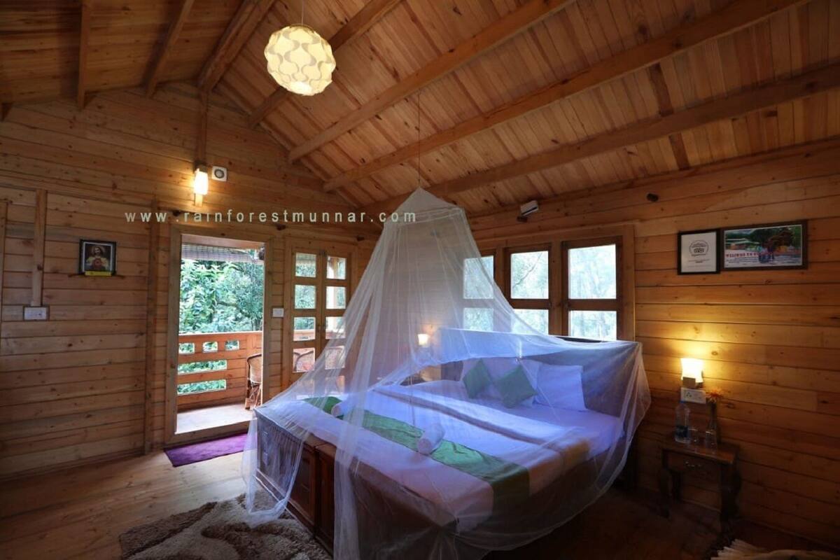 Un dormitorio de cabaña de madera con cama con dosel, techo de madera y ventana con vista a follaje.