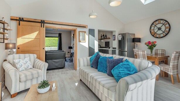 A spacious living room with a sofa, chairs, a coffee table, and a dining area. There is a kitchen in the background with a refrigerator and a clock on the wall. - 2 bedroom accommodation in Chapel St Leonards, near Skegness (Chapel St Leonards, near Skegness)
