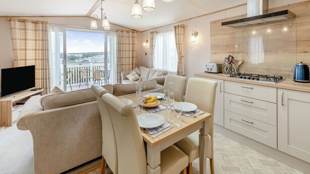 A modern kitchen with a gas stove, a dining table set for two, and a sofa in the living area. - 3 bedroom accommodation in Weymouth (Weymouth)