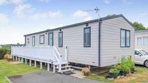 A mobile home with a covered porch, a satellite dish, and a car parked nearby. - 3 bedroom accommodation in Weymouth (Weymouth)