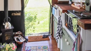 A cozy kitchen with a stove, a kettle, and a view of a green field through a window.