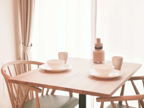 A wooden table with two white plates and two white cups, a woven bottle, and a wooden chair.