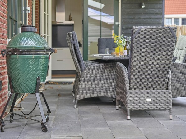 An outdoor patio with a green barbecue grill on wheels, wicker furniture, and a table with a vase of flowers.
