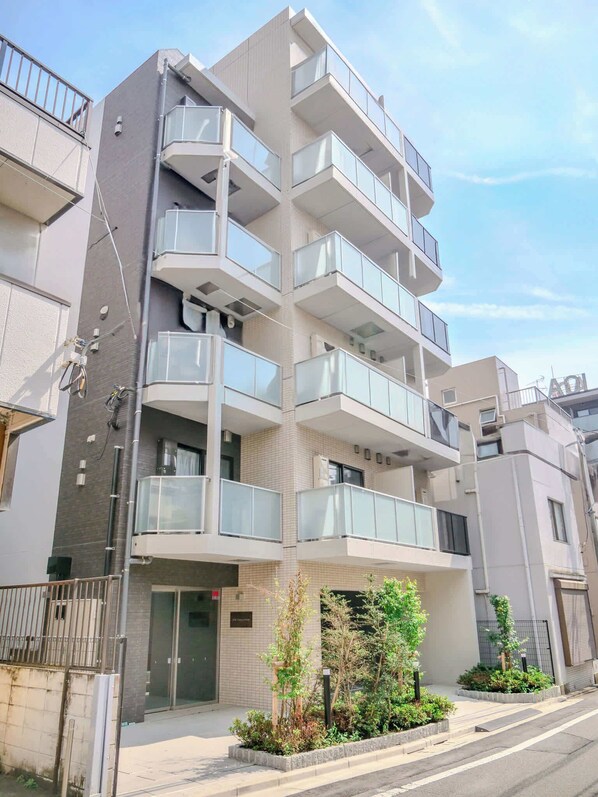 A multi-story residential building with balconies, a gated entrance, and a small garden area.