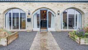 Un bâtiment en pierre avec une entrée centrale, de grandes fenêtres en arc de cercle et un chemin de gravier menant à la porte.