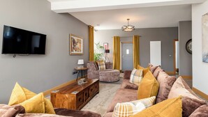Ein Wohnzimmer mit Flachbildfernseher, Couchgarnitur, Holztisch und einer Tür zu einem anderen Raum.
