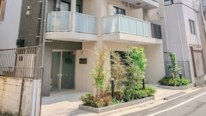 Un immeuble résidentiel à plusieurs étages, doté de balcons, d’une entrée sécurisée et d’un petit jardin.
