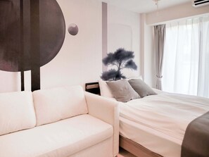 Una habitación de hotel moderna con un sofá blanco, una cama con ropa de cama blanca y un cuadro abstracto grande en la pared.