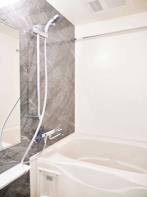 Une salle de bain avec un mur en marbre, une baignoire et une douche équipée d’un pommeau de douche amovible.