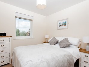 Un dormitorio con una cama, ventana, mesita de noche, lámpara, cómoda y un cuadro en la pared.