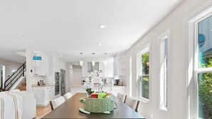 Une cuisine moderne avec des meubles blancs, une table à manger avec des chaises et un escalier menant à un autre niveau.