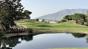Ein Golfplatz mit Teich, Bäumen und Bergen im Hintergrund.