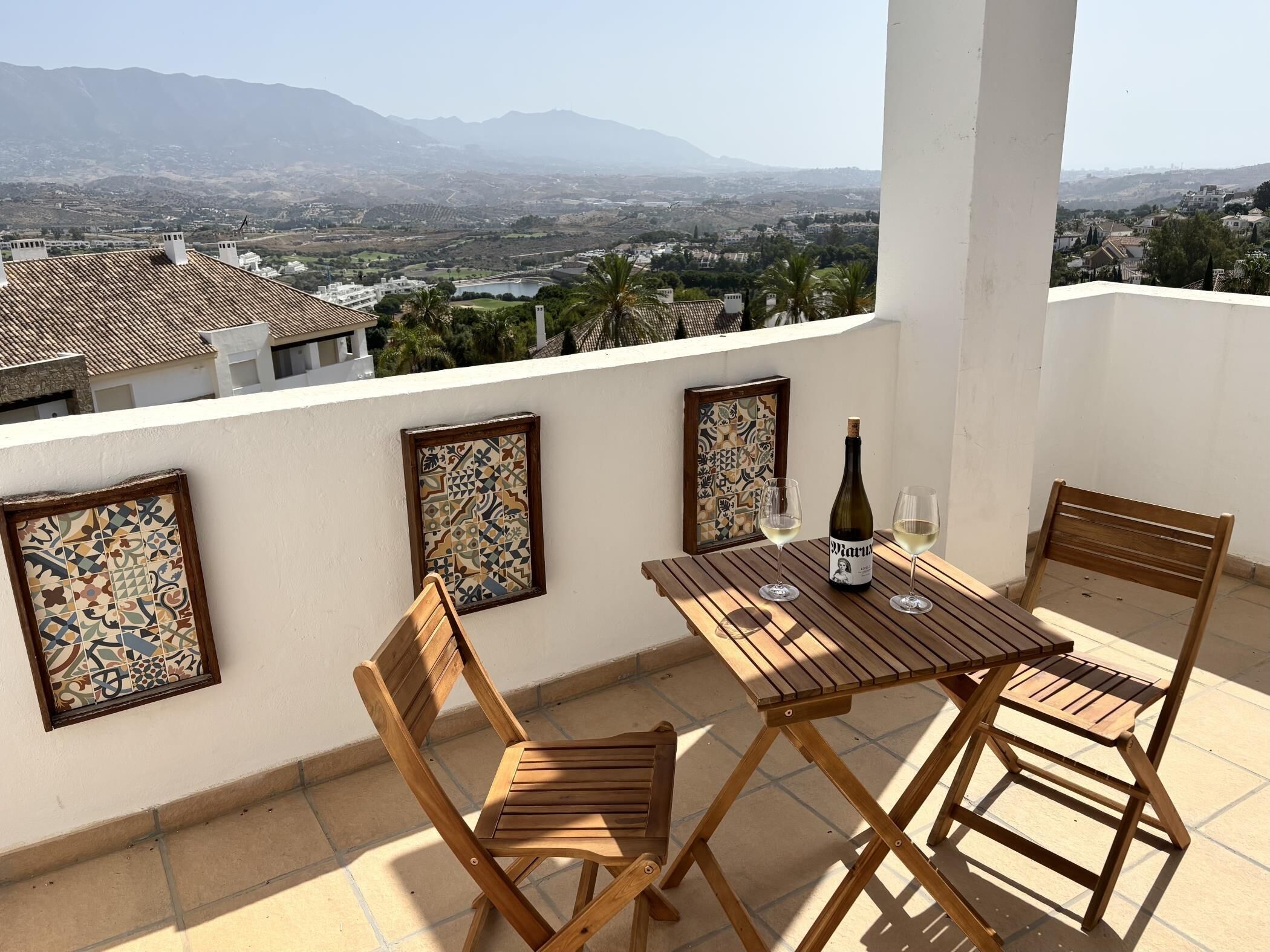 A balcony with a table, two chairs, a bottle of wine, and two glasses.