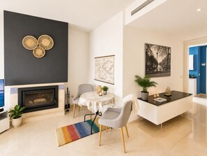 A modern living room with a fireplace, a dining area with a table and chairs, and a kitchen area with a white cabinet.
