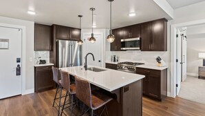 Una cocina moderna con armarios de madera oscura, una isla grande con taburetes de bar, electrodomésticos de acero inoxidable e iluminación colgante.