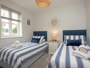 Quarto com duas camas, mesa de cabeceira com abajur, espelho e janela com persianas.