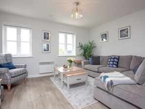 A modern living room with a sofa, armchair, coffee table, and a radiator. - 3 bedroom accommodation in Brixham (Brixham)