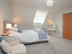 A bedroom with a bed, bedside table, lamp, chair, and a wooden wardrobe.