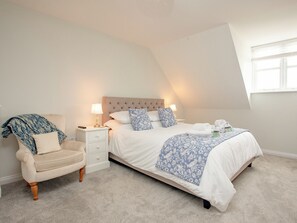 Ein Schlafzimmer mit Bett, Nachttisch, Sessel und Fenster.