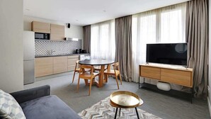 A modern living room with a sofa, a dining table with chairs, a TV, and a kitchen area with cabinets and a microwave. - Appartement cosy - Porte de Versailles (Paris)
