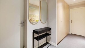 A hallway with a black console table, two large mirrors, and a door with a cityscape view. - Appartement cosy - Porte de Versailles (Paris)