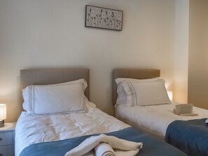 Deux lits jumeaux avec des têtes de lit, une literie blanche, une couverture bleue, une serviette blanche, une table de chevet avec une lampe et un tableau encadré au mur.