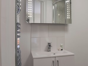 Uma casa de banho com uma pia branca, um espelho com luzes e um dispensador de toalhas.
