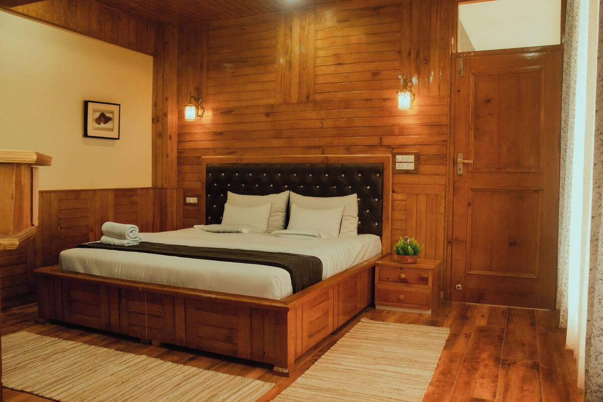 Ein schlafzimmer mit Holzwandverkleidung, einem großen Bett, einem Nachttisch mit Pflanze und einer Tür.